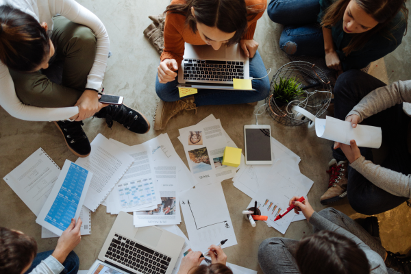 Group of people sitting on the floor, surrounded by papers and laptops
